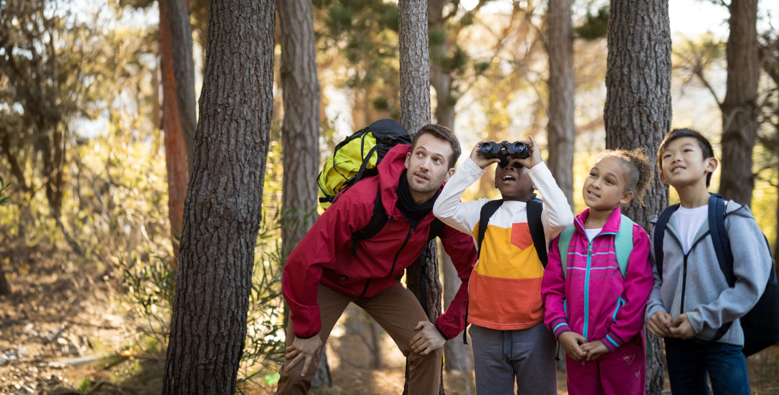 A teacher and three students scouting with binoculars